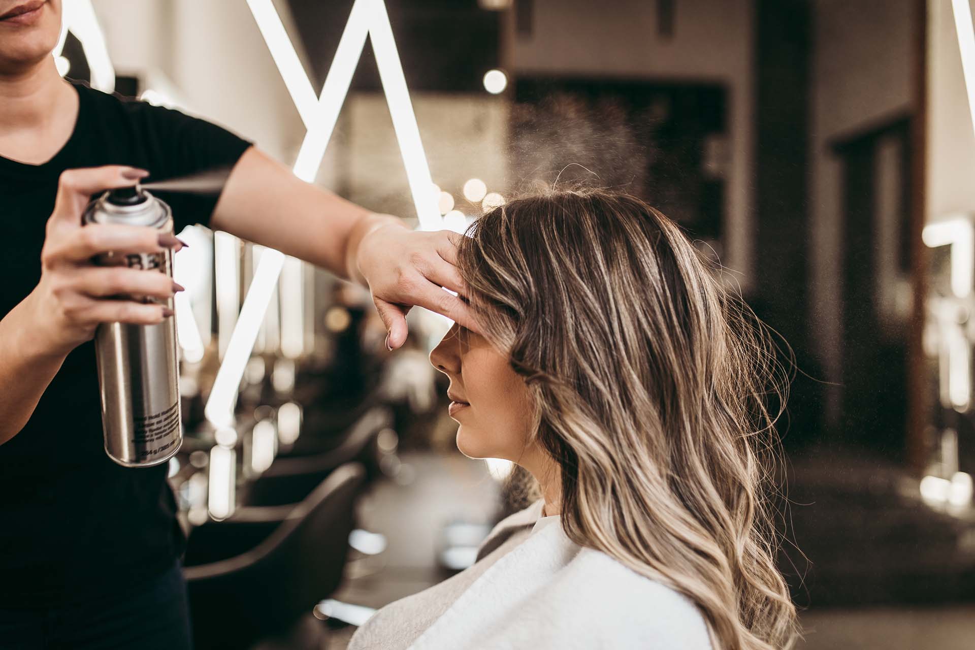 En stylist sprayar hårspray på en kvinnas hår